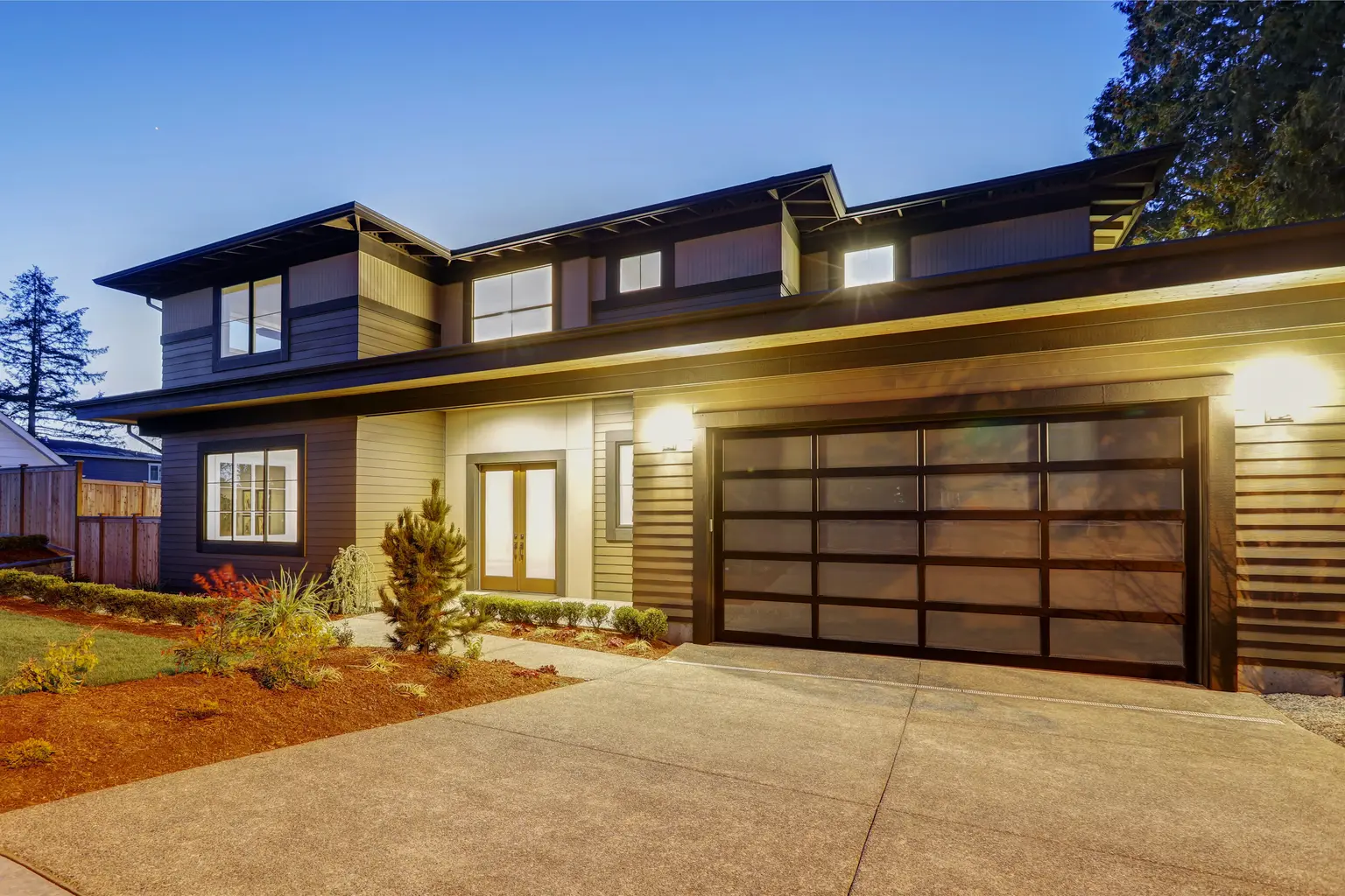 Modern two-storey home with a glass garage door at dusk